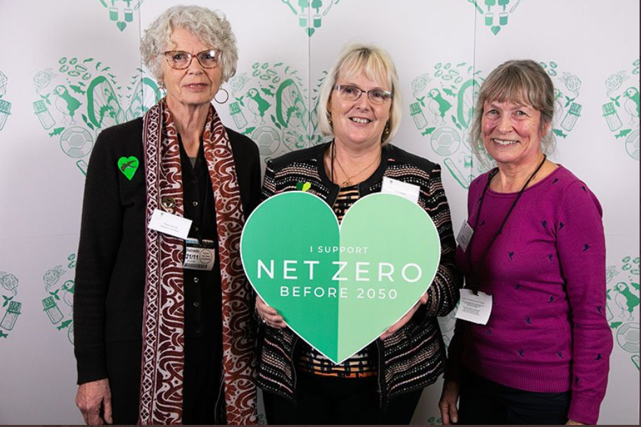 3 women standing next to each other with the one in the middle (Ann Jones) holding a green heart made of carton