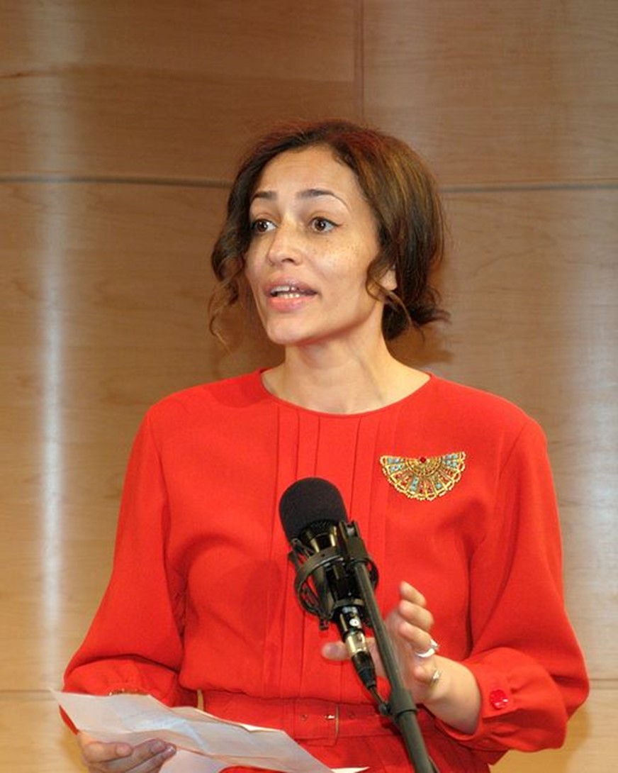 Zadie Smith standing behind a microphone and speaking while holding a piece of paper 