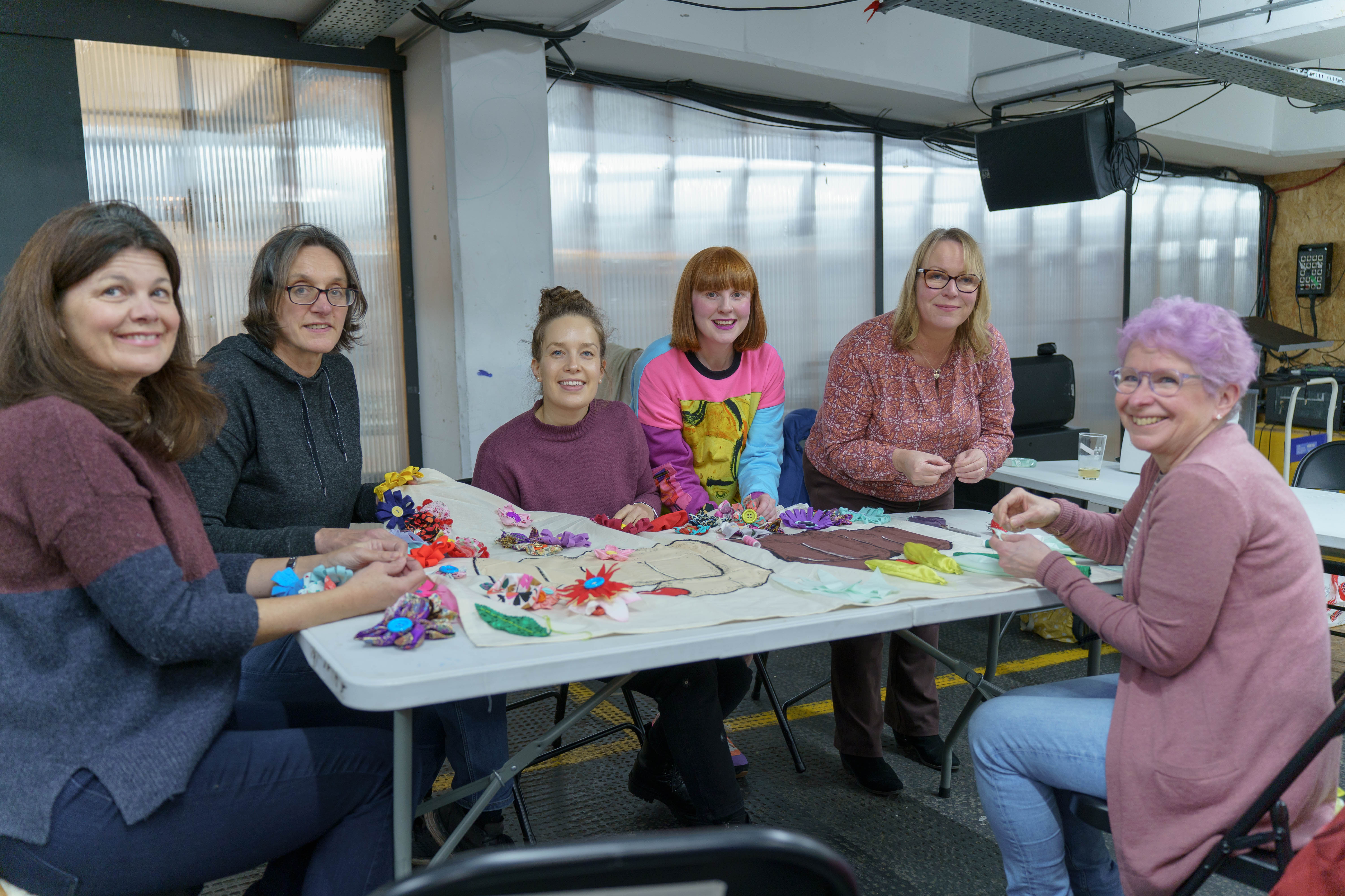 A group of women sat around a table doing arts and crafts.