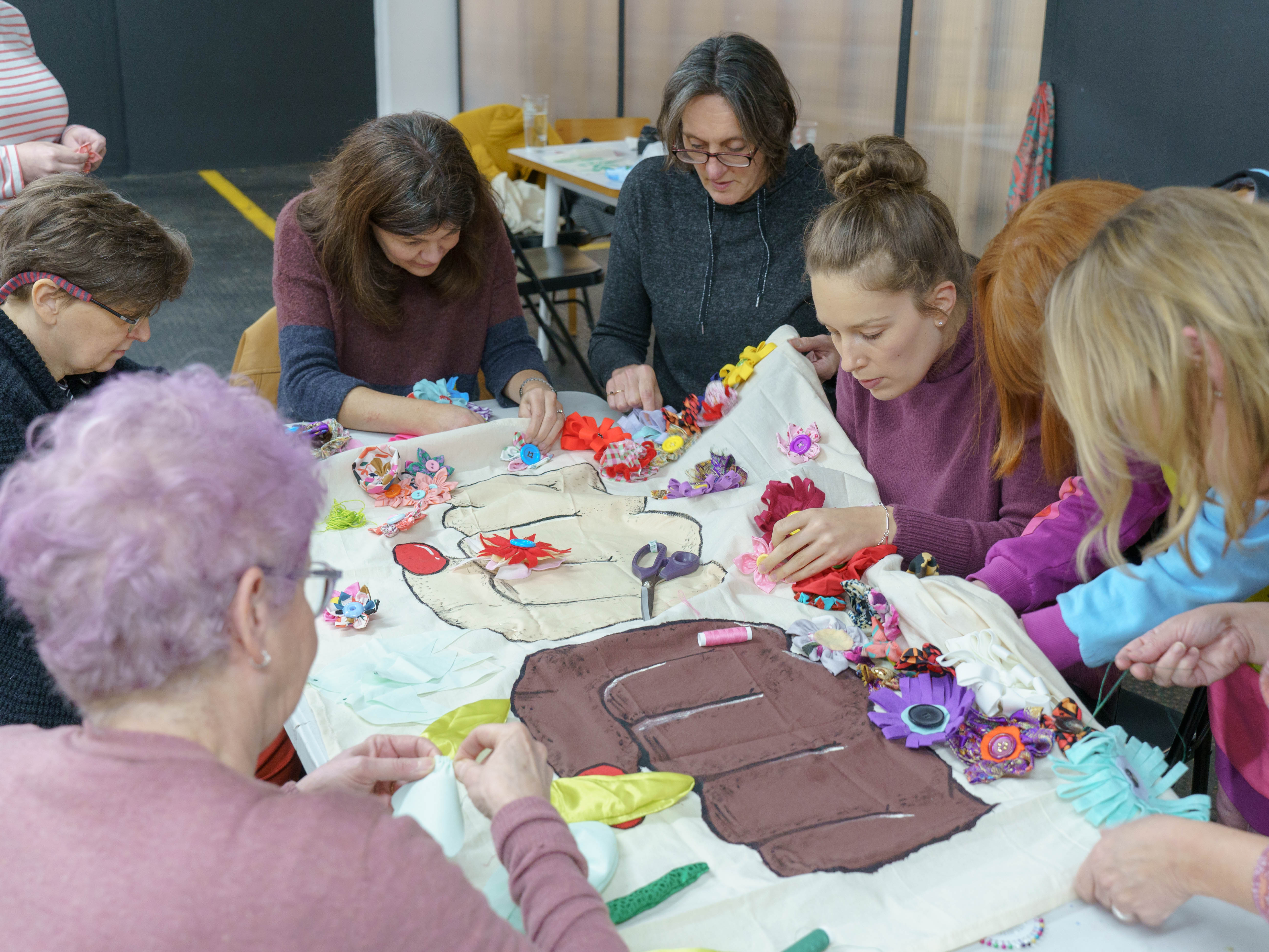 A group of women sat around a table making a sign together.