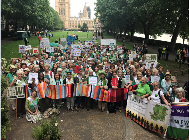 A large group of women/WI members standing together outside holding up banners/placards at the Climate Change Mass Lobby