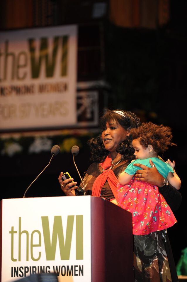 Dr Aderin-Pocock on stage at the NFWI Annual Meeting, speaking and holding a child in her arms